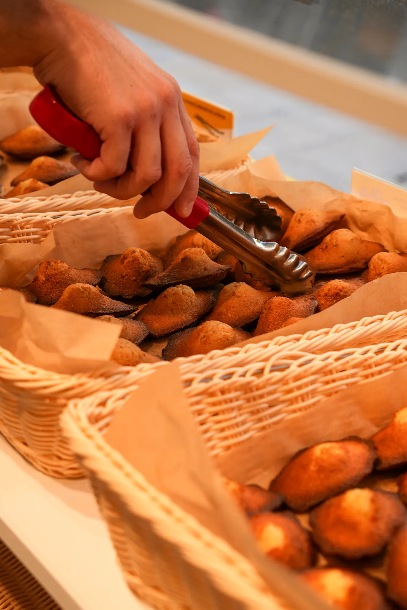 Madeleines servies à la pince dans une boutique artisanale